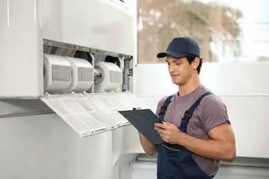 Photo of Technician with clipboard near air conditioner indoors