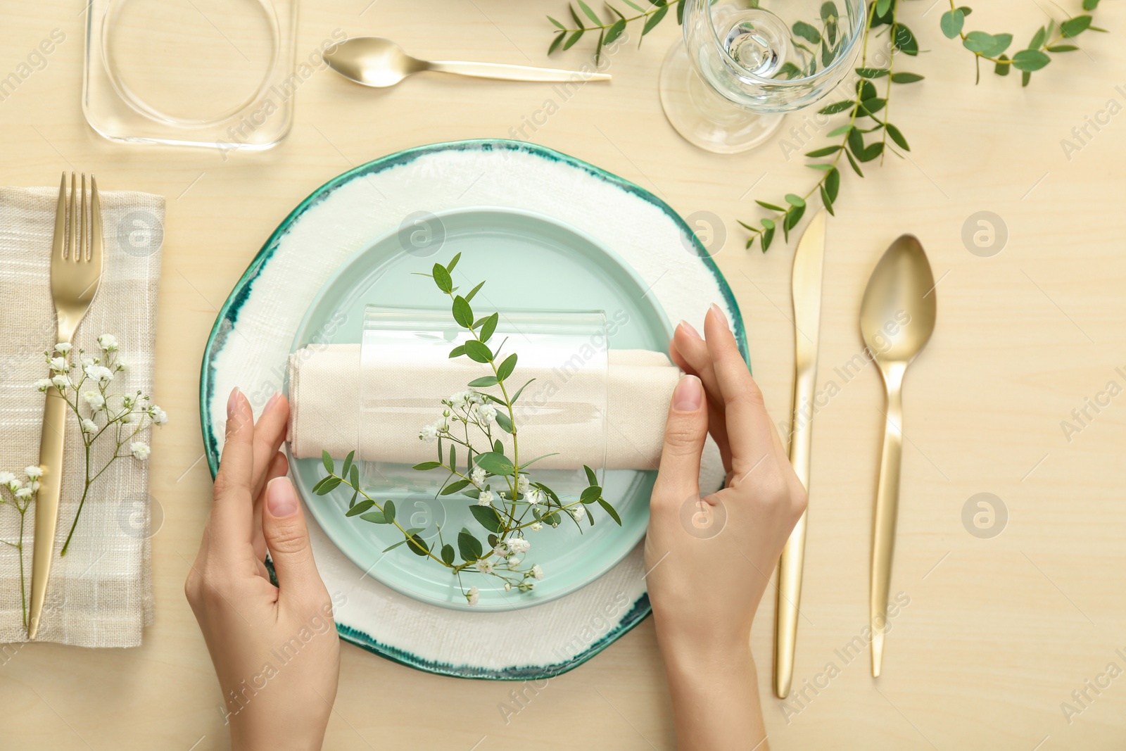 Photo of Woman setting table with green leaves for festive dinner, top view