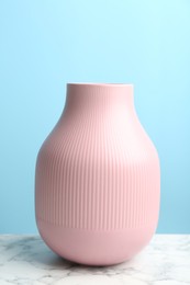 Stylish pink ceramic vase on white marble table against light blue background
