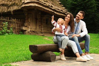 Photo of Happy family in Ukrainian national clothes sitting on bench outdoors