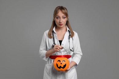 Photo of Woman in scary nurse costume with pumpkin bucket on light grey background. Halloween celebration
