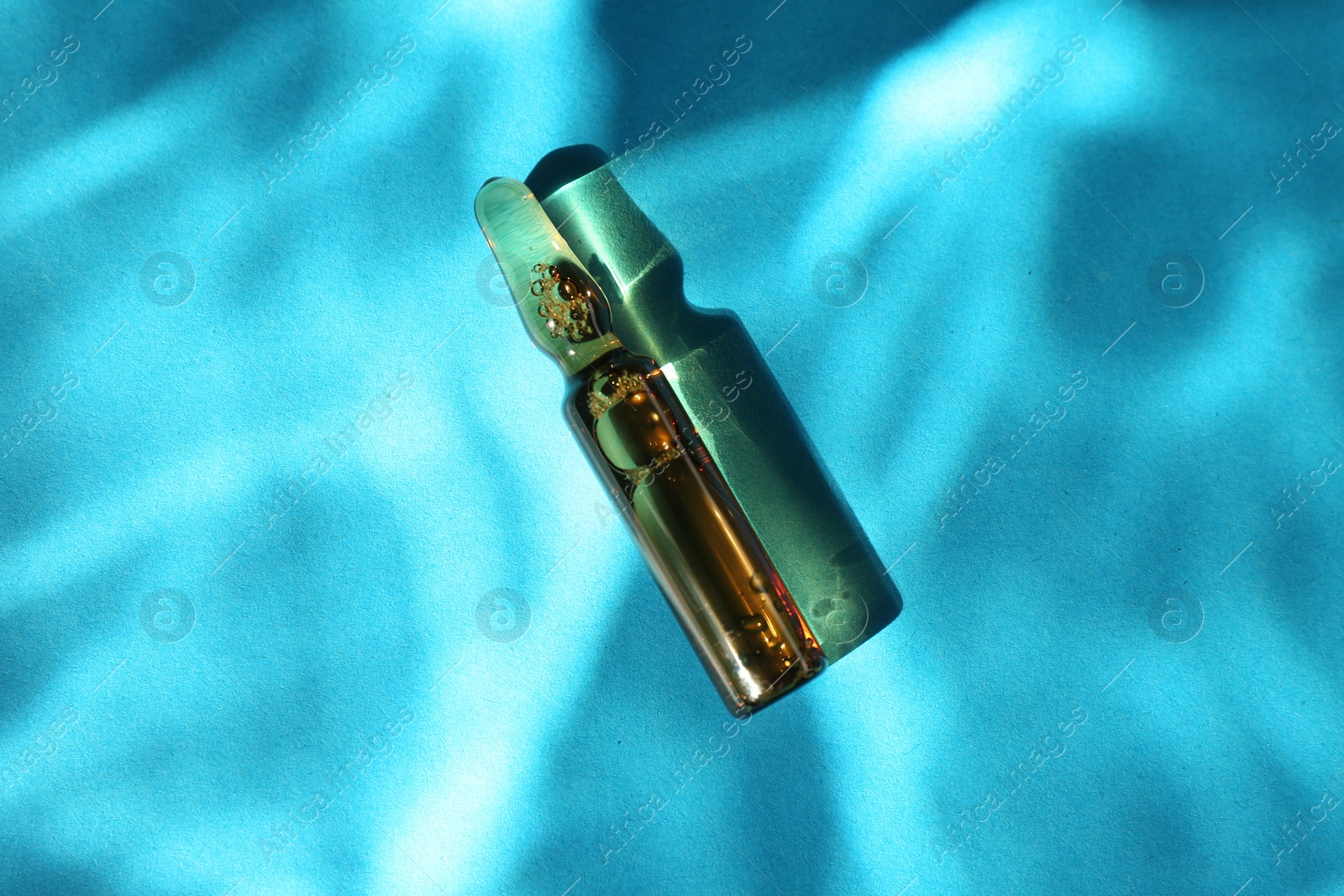 Photo of Skincare ampoule in sunlight on light blue background, top view