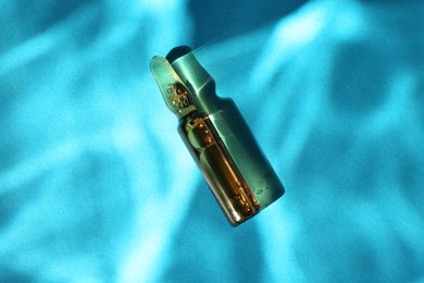 Skincare ampoule in sunlight on light blue background, top view