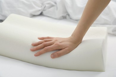 Woman touching orthopedic memory foam pillow on bed, closeup. Space for text