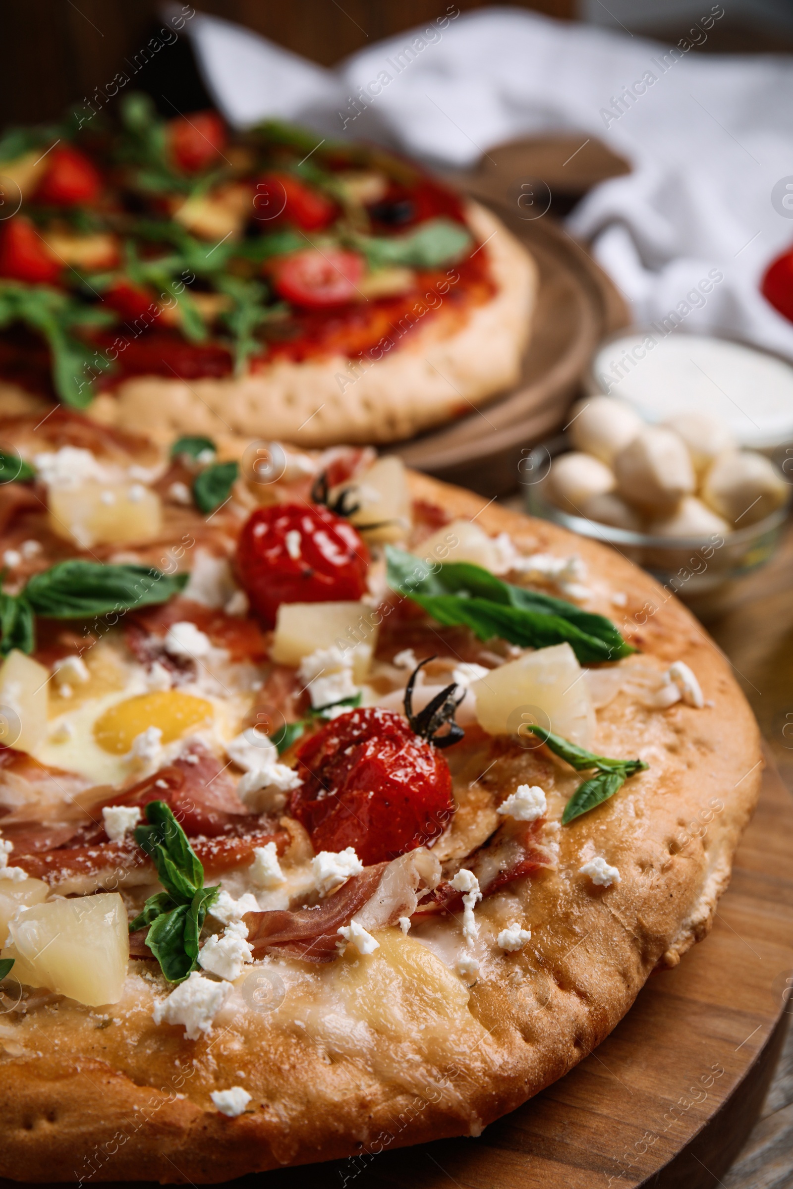 Photo of Pita pizza with prosciutto, pineapple, grilled tomatoes and egg on wooden tray, closeup