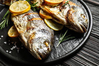 Photo of Delicious roasted fish with lemon on black wooden table, closeup