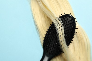 Photo of Stylish brush with blonde hair strand on light blue background, top view. Space for text