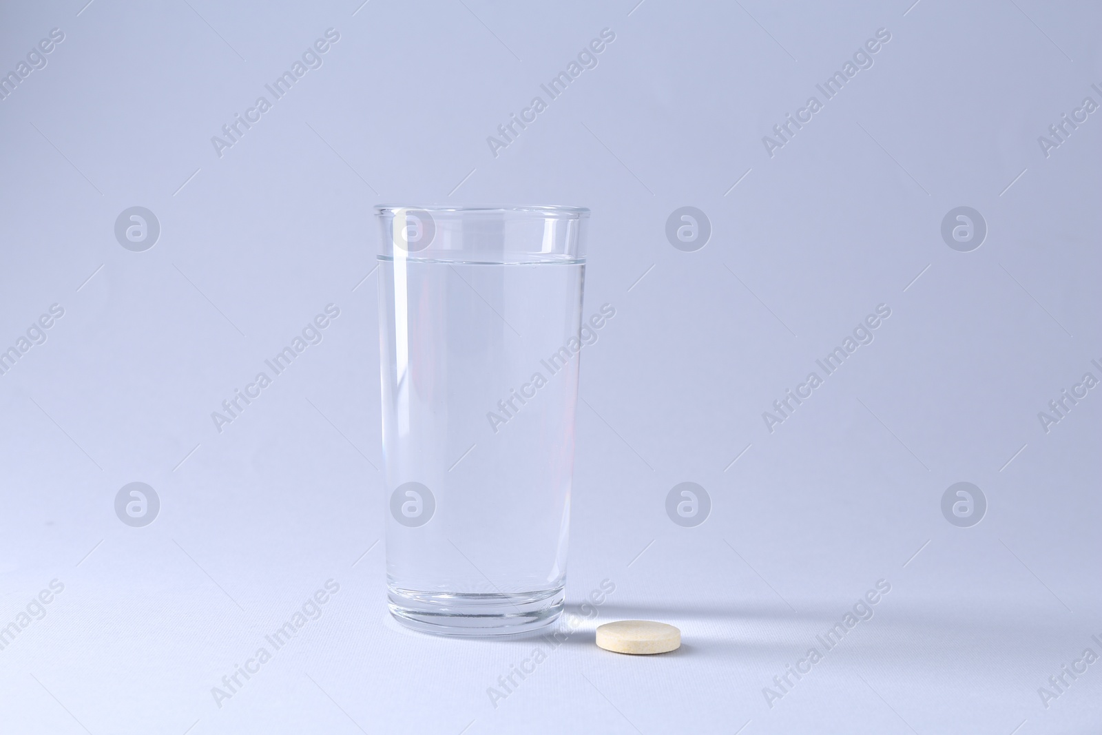 Photo of Effervescent pill and glass of water on light grey background