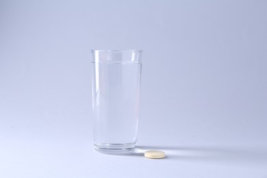 Effervescent pill and glass of water on light grey background