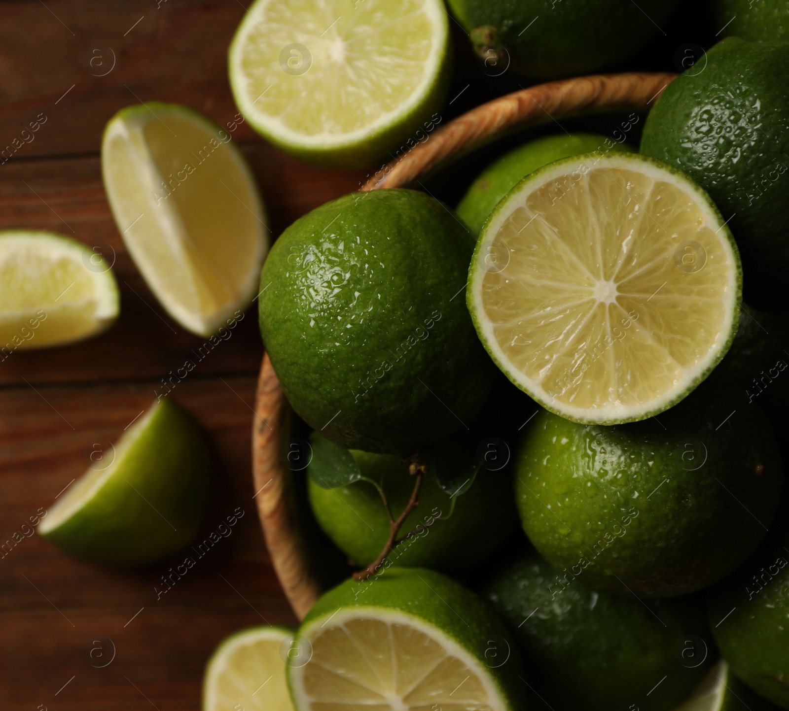 Photo of Fresh whole and cut limes with water drops on wooden table, flat lay