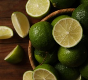 Photo of Fresh whole and cut limes with water drops on wooden table, flat lay