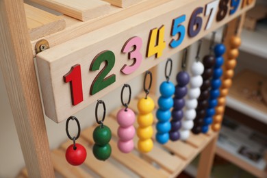 Photo of Montessori toy with color bead lines and numbers on wooden stand in room, closeup