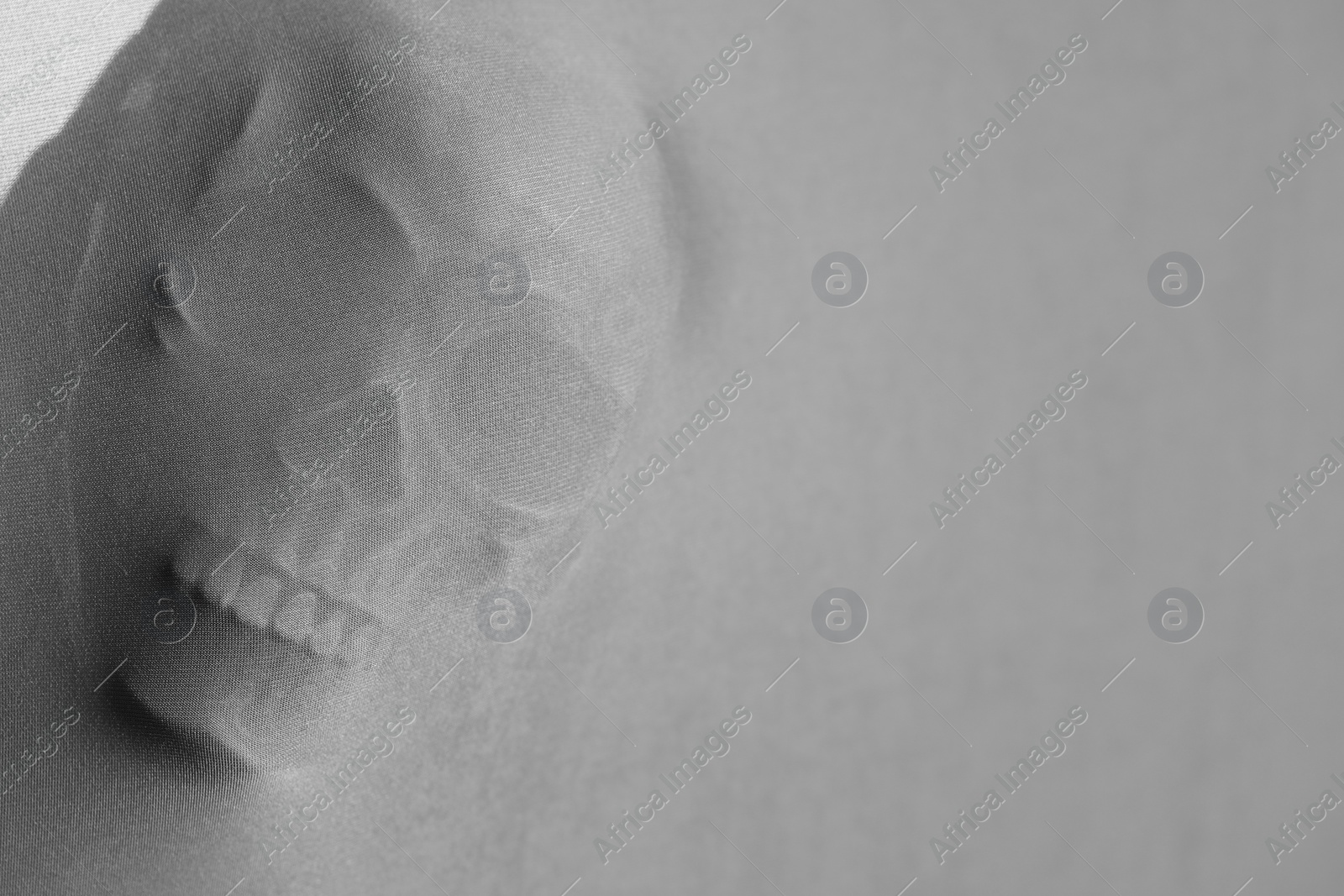 Photo of Silhouette of creepy ghost with skull behind cloth, space for text. Black and white effect