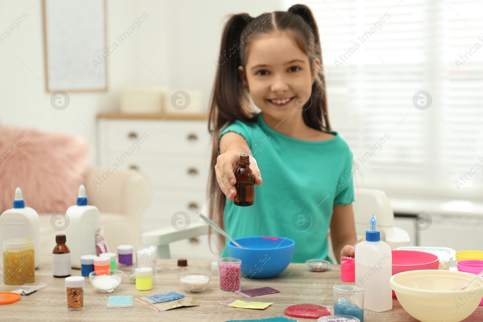 Photo of Cute little girl making slime toy at table indoors