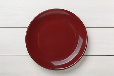 Photo of Empty burgundy ceramic plate on white wooden table, top view