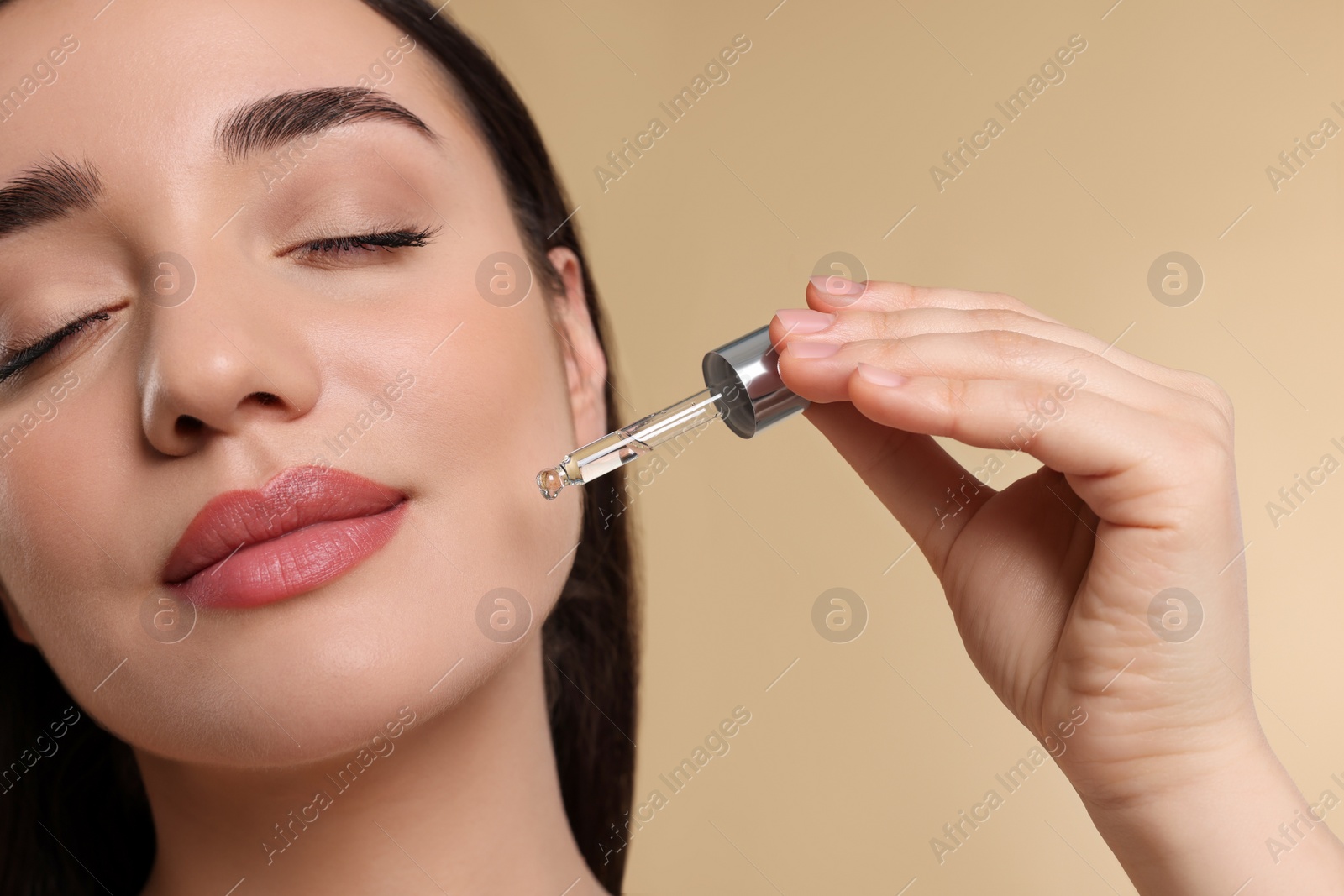 Photo of Young woman applying essential oil onto face on beige background, closeup