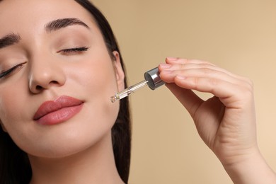 Photo of Young woman applying essential oil onto face on beige background, closeup