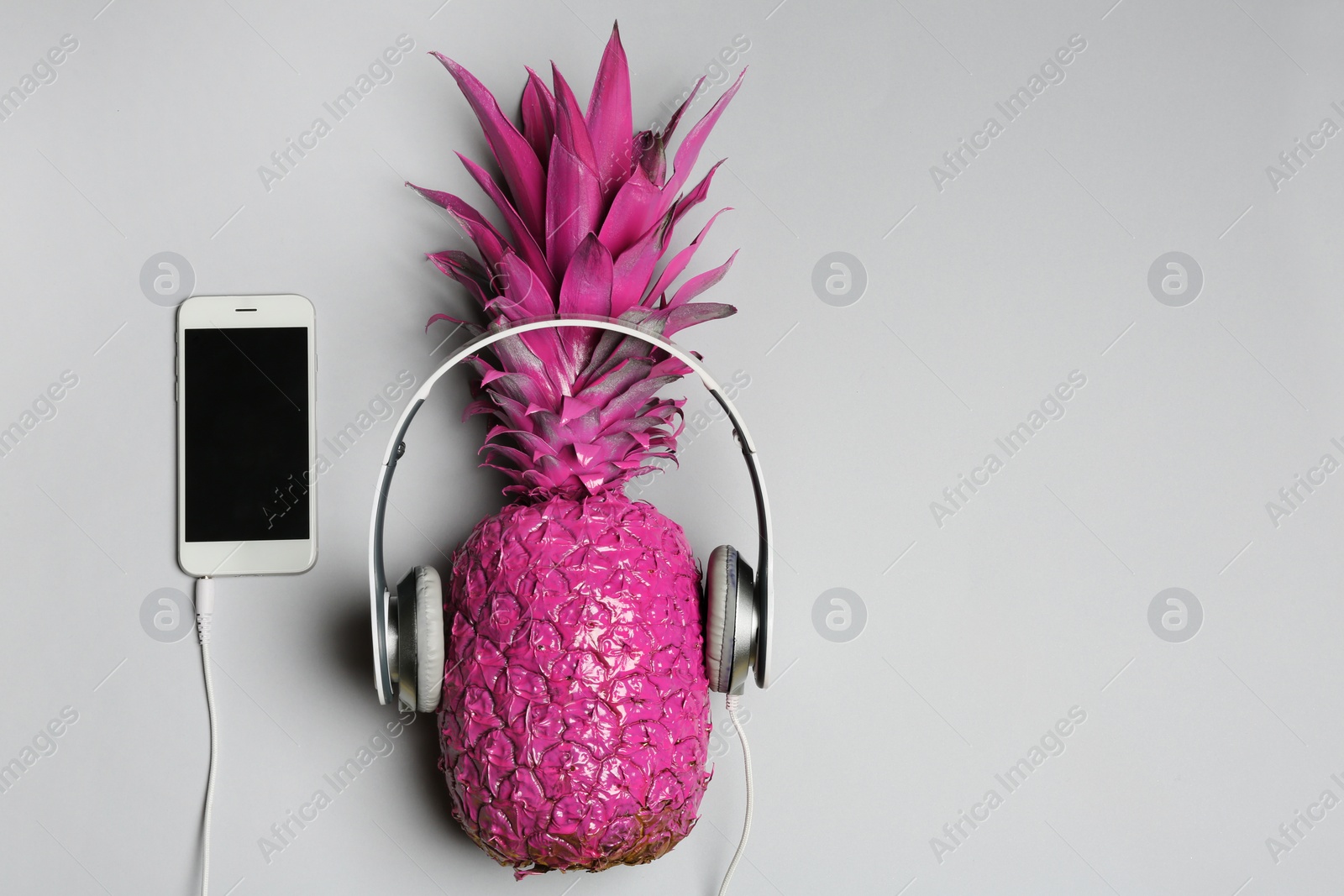 Photo of Pineapple with headphones and smartphone on grey background, top view with space for text