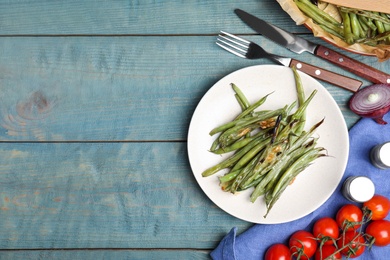 Photo of Delicious baked green beans served on light blue wooden table, flat lay. Space for text
