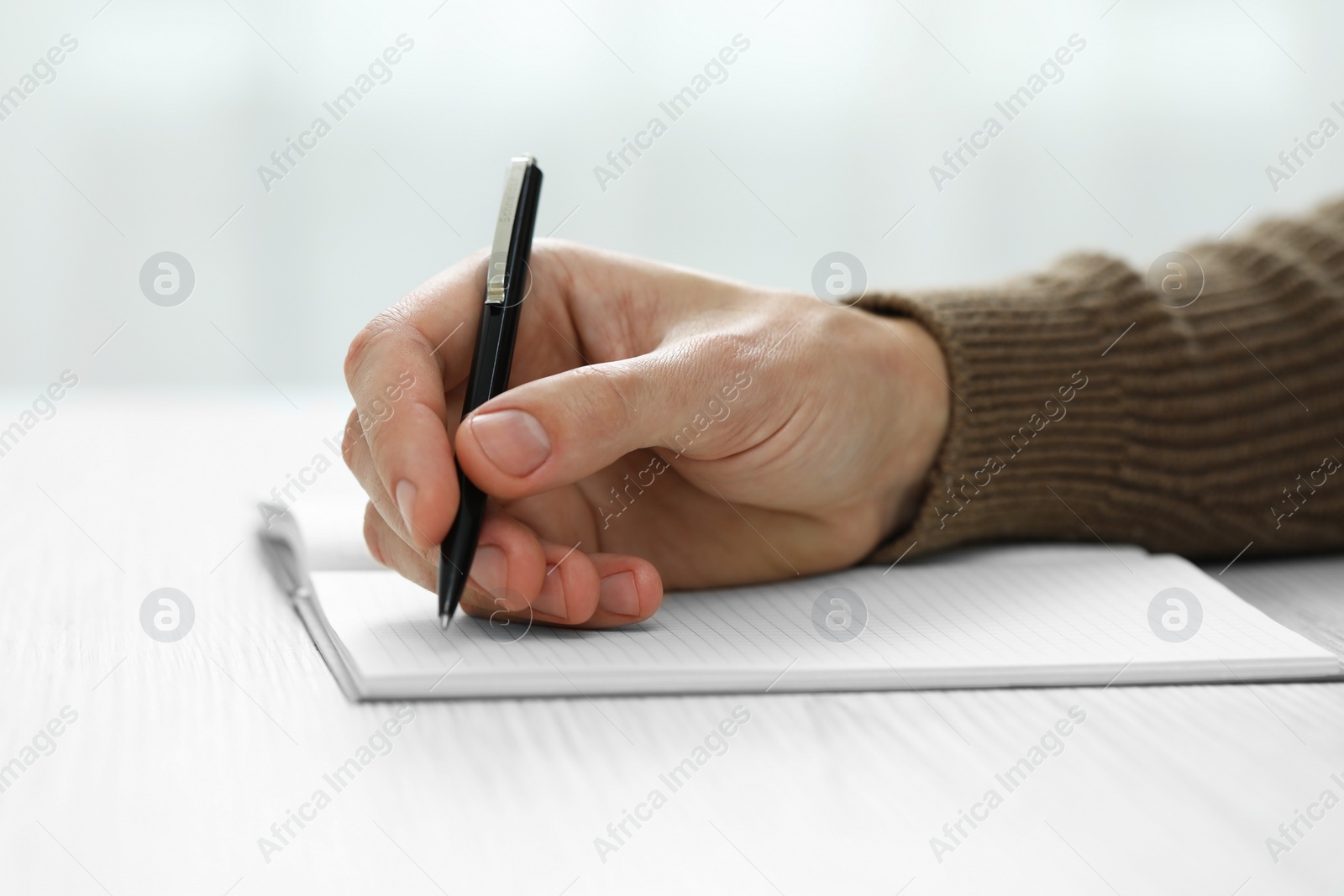 Photo of Man writing in notebook at white wooden table, closeup