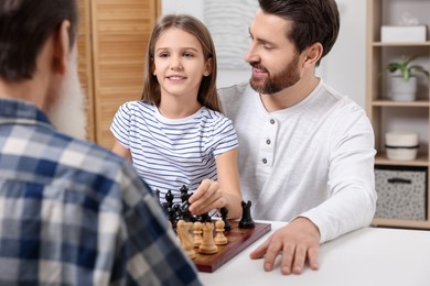 Photo of Family playing chess together at table in room