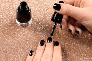 Photo of Woman applying black nail polish on shiny color background, closeup