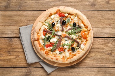 Photo of Tasty pizza with anchovies, arugula and olives on wooden table, top view