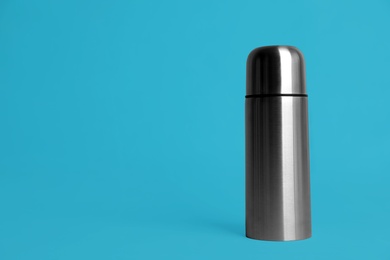 Photo of Stylish thermo bottle on light blue background, space for text