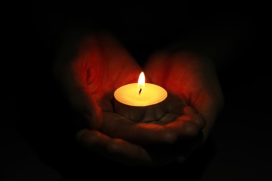 Photo of Woman holding burning candle in darkness, closeup