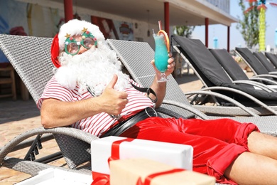 Authentic Santa Claus with cocktail resting on lounge chair at resort