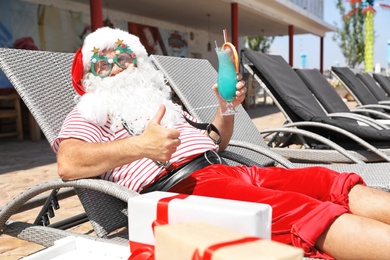 Photo of Authentic Santa Claus with cocktail resting on lounge chair at resort