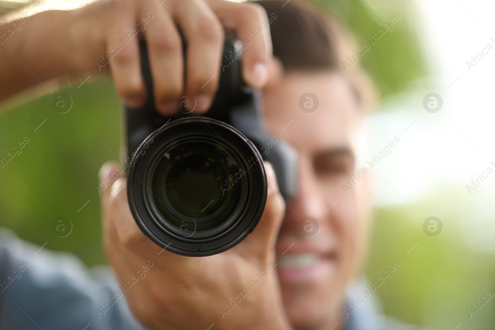 Photo of Photographer taking picture with professional camera outdoors, focus on lens
