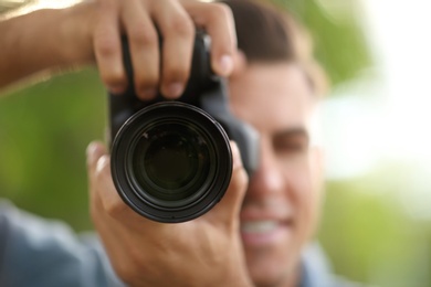 Photographer taking picture with professional camera outdoors, focus on lens