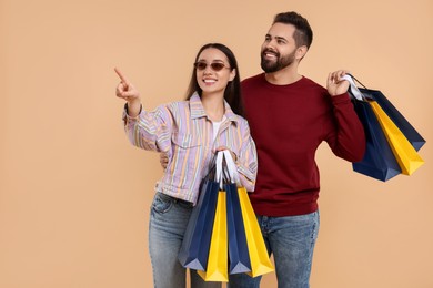 Happy couple with shopping bags looking at something on beige background. Space for text