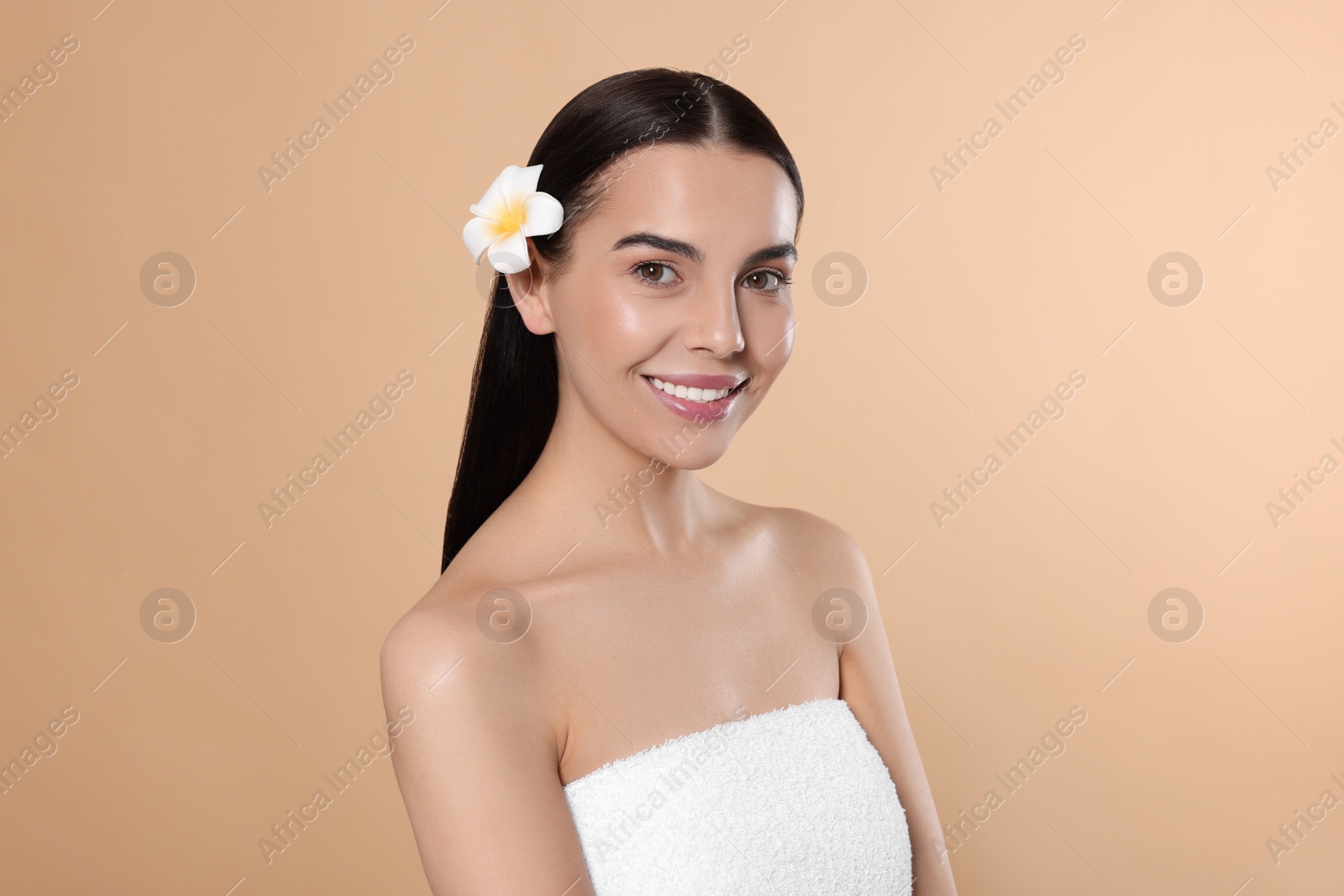 Photo of Young woman with plumeria flower in hair on beige background. Spa treatment