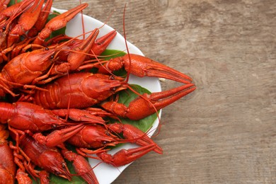 Plate with delicious red boiled crayfish on wooden table, top view