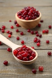 Photo of Spoon with fresh ripe cranberries on wooden table, closeup