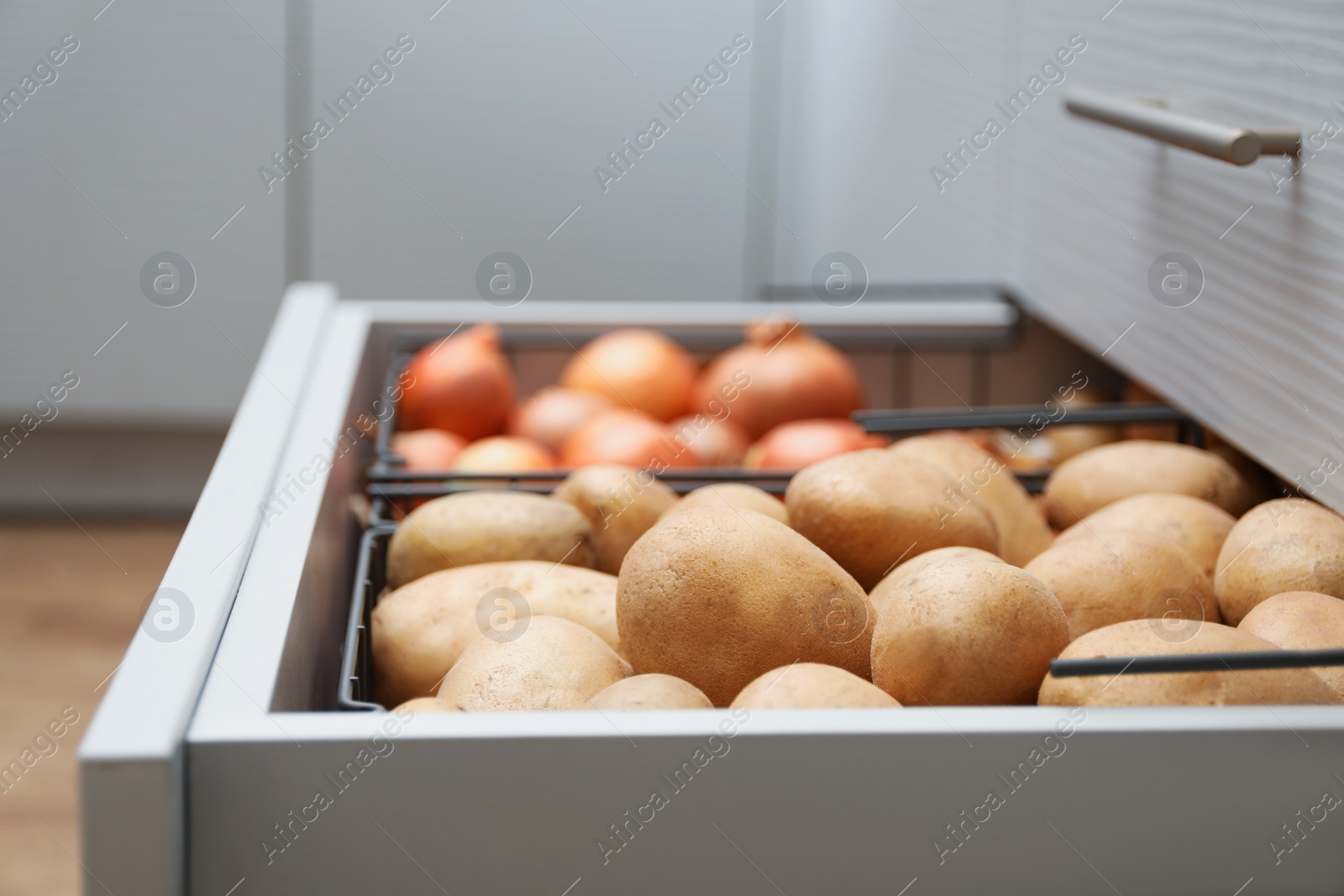 Photo of Open drawer with potatoes and onions in kitchen. Orderly storage