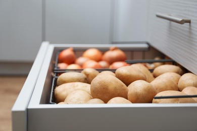 Open drawer with potatoes and onions in kitchen. Orderly storage