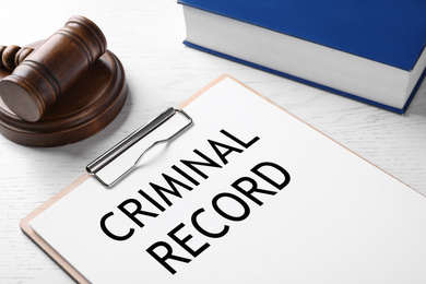 Clipboard with words CRIMINAL RECORD and gavel on white wooden table, closeup