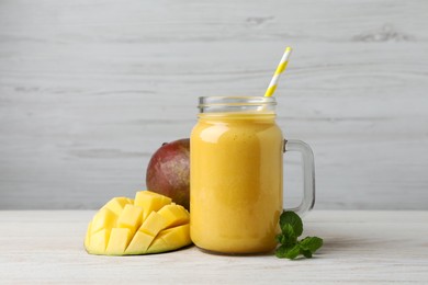 Photo of Mason jar with delicious fruit smoothie and fresh mango on white wooden table