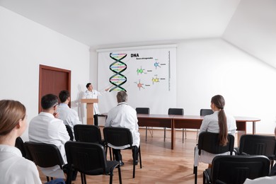 Image of Lecture about nucleobases of DNA. Professor using projection screen with illustration to audience in conference room