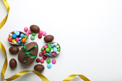 Photo of Delicious chocolate eggs with green bow, sweets and golden ribbon on white background, flat lay. Space for text