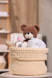 Photo of Knitted basket with baby cosmetic products, bath accessories and toy bear on white table indoors