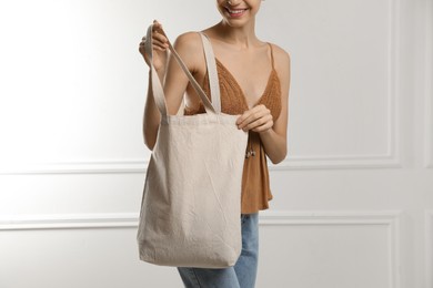 Happy young woman with blank eco friendly bag near white wall, closeup