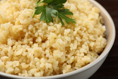 Photo of Delicious bulgur with parsley in bowl, closeup