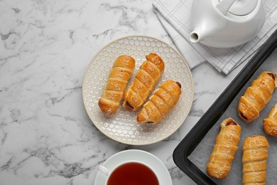 Photo of Delicious sausage rolls and hot drink on white marble table, flat lay. Space for text