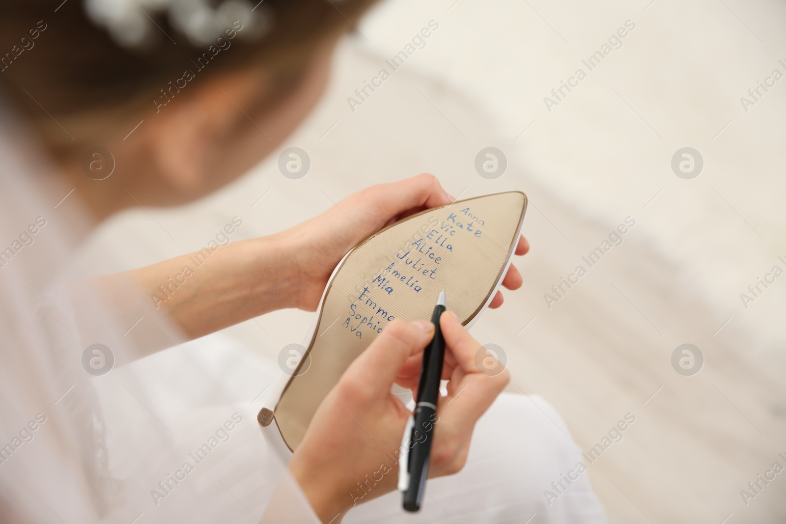 Photo of Young bride writing her single friends names on shoe indoors, above view. Wedding superstition