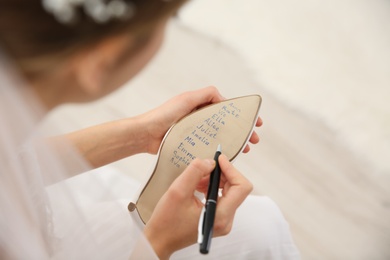 Young bride writing her single friends names on shoe indoors, above view. Wedding superstition