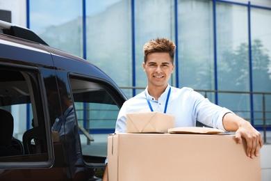 Young courier with parcels near delivery car outdoors